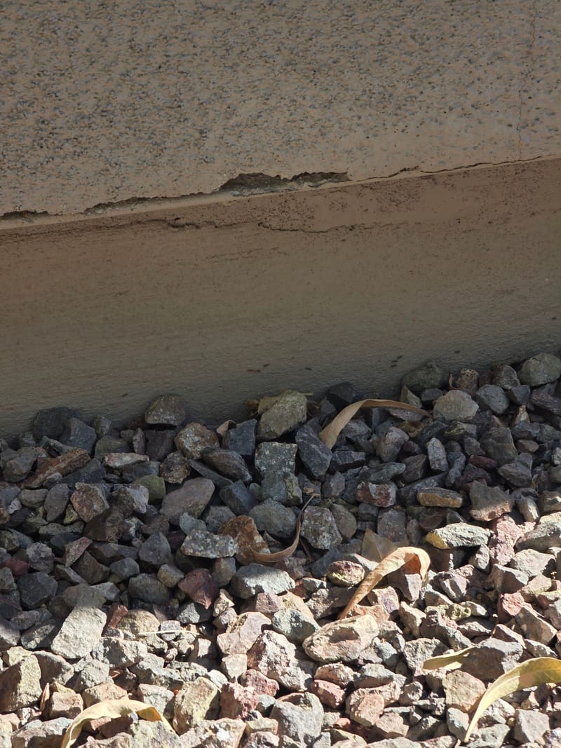 Cracked stucco along the foundation line above a gravel bed