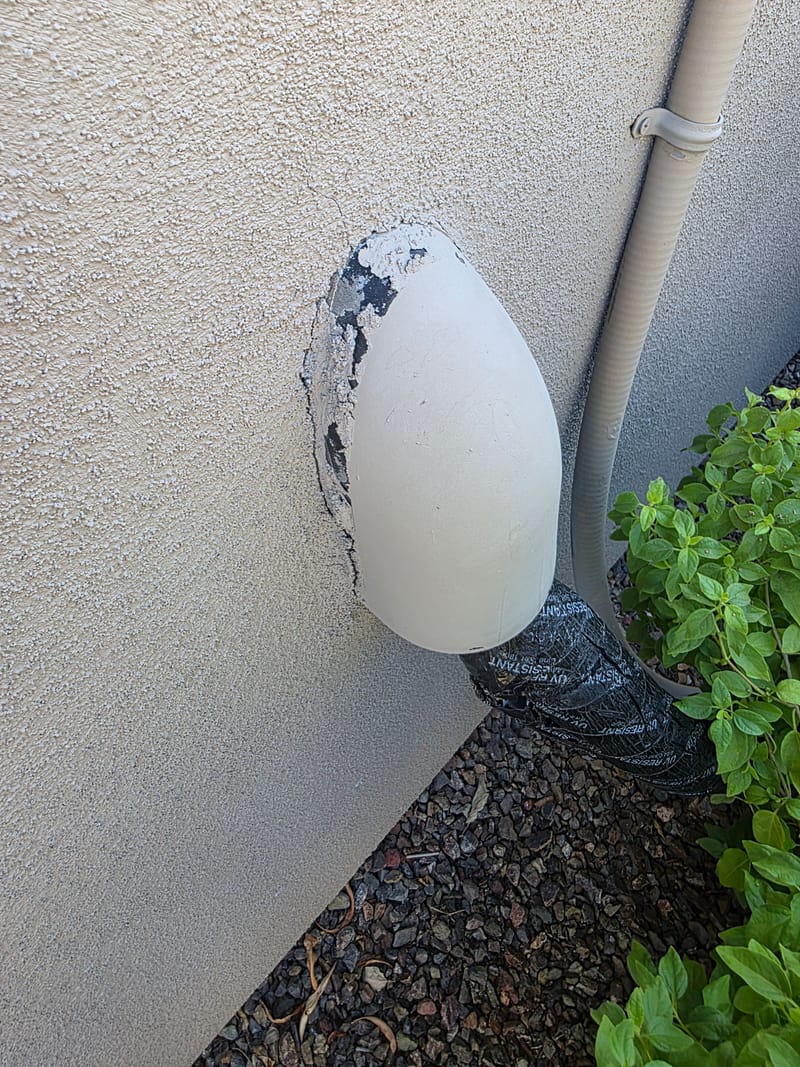 Cracked and chipped stucco around a wall mounted light fixture wrapped in black UV resistant tape